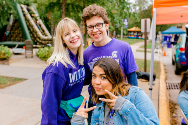 Three students pose smiling at a campus event.