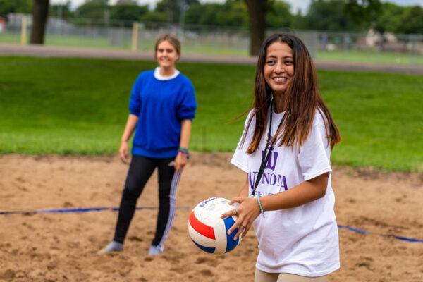 A female student holds a volleyball while standing on a sand volleyball court on WSU campus.