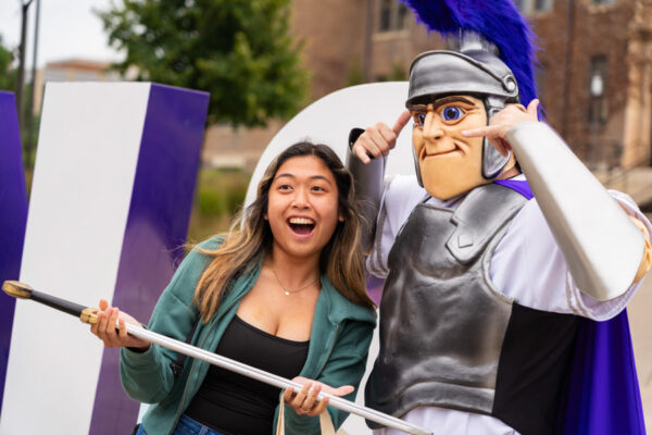 A student holds a prop sword while posing with the Wazoo mascot by the WSU letters on the Winona campus.