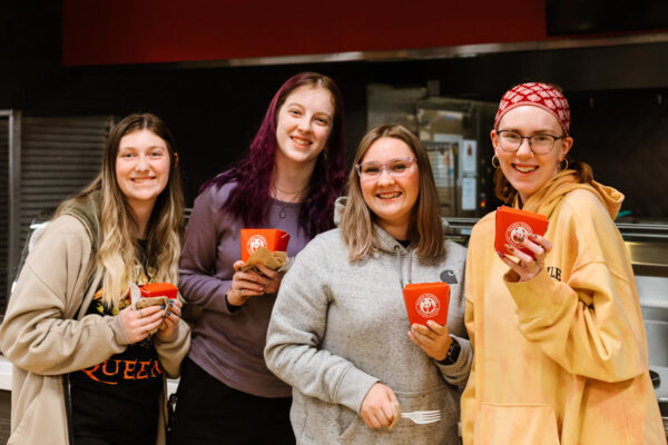Four students smile and pose while holding cartons from Panda Express during an event.