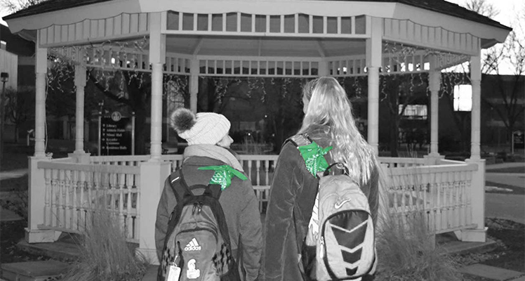 Students standing in front of gazebo with green bandanas tied to their backpacks