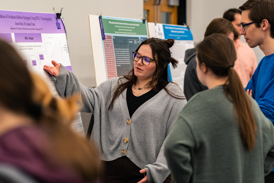 A female student explains a research project to a group of people. 