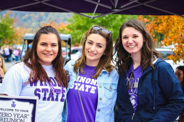 A group of female alumni wearing WSU merch pose together at an event on WSU campus.