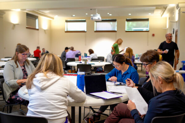 Students work on laptops in a large classroom space.