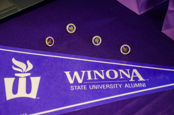 A purple WSU pennant flag lays next to several WSU Alumni pins on a table.