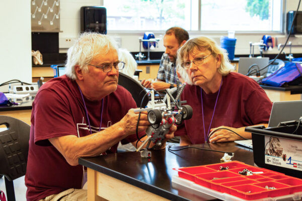 Two older adults work together to assemble a robotics car during a class.