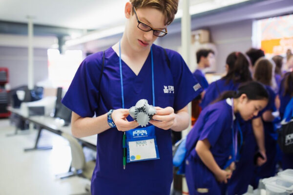 A high school student wearing scrubs looks at a medical device during Scrubs Camp at WSU campus.