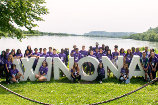 Staff and students in the HOPE Academy program pose together by letter signs that read Winona in front of a lake.