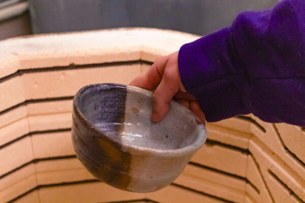 A student removes a finished ceramic bowl from a kiln.
