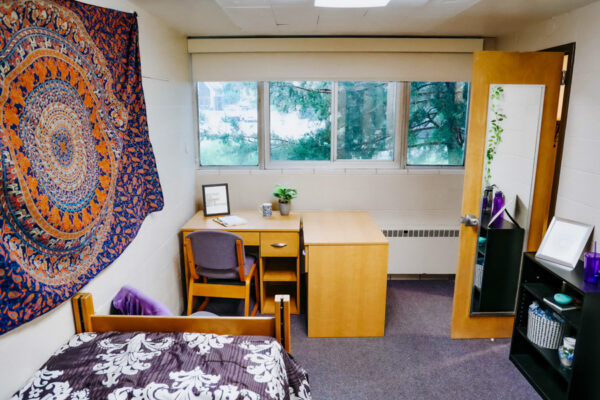 A room with a bed along the wall and desk placed under the windows in Conway Hall.