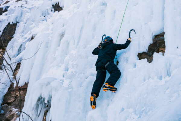 A person in full gear climbs up an ice wall.