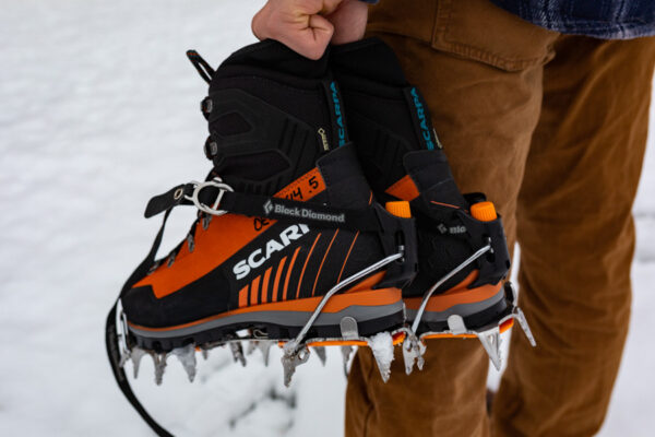 A person carries a pair of ice climbing boots.