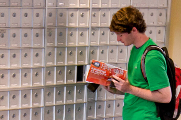 A student opens their private mailbox in the mail area of Kirkland-Haake Hall.