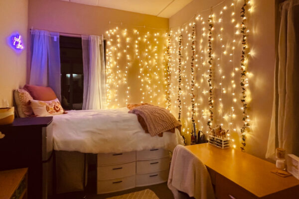 A room with a lofted bed that has storage below and curtain lights hanging along the wall in Kirkland-Haake Hall.