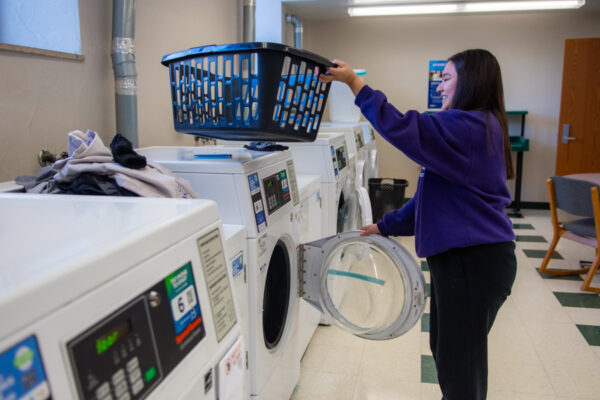 A student takes laundry out of a dryer in the laundry room in Morey-Shepard Hall.