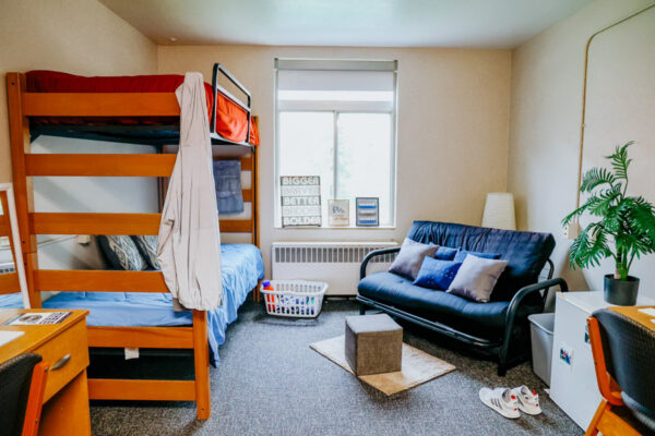 A room with bunk beds and small living area with a futon near the windows in Morey-Shepard Hall.