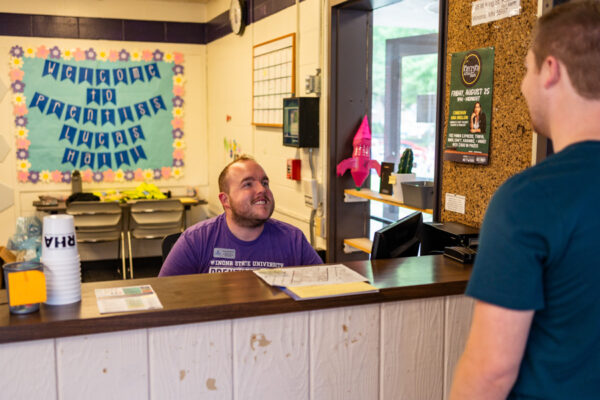 A student worker greets a student as the front desk in Prentiss-Lucas Hall.