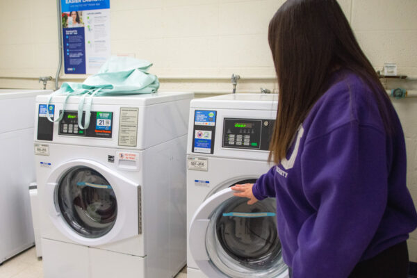 A student opens a washing machine in the laundry room in Richards Hall.