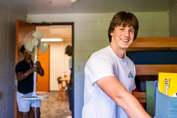 Two male student carry belongings into a residence hall room in Richards Hall.