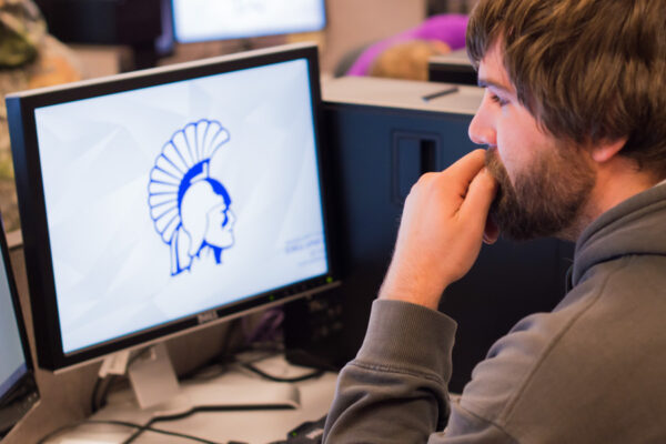 A male student uses a desktop computer in an office space.