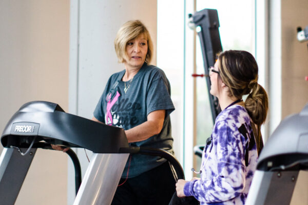 A student trainer works with a woman on a treadmill in a fitness center.