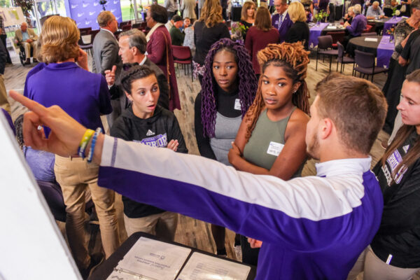 A group of students talk to a presenter at a campus event.