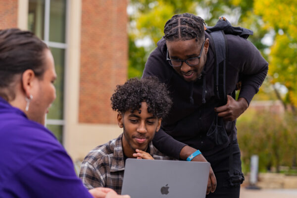 Two student look at a laptop together while sitting at a table outside on the WSU campus.