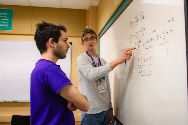 A peer tutor writes on a whiteboard to explain a concept to a WSU student.