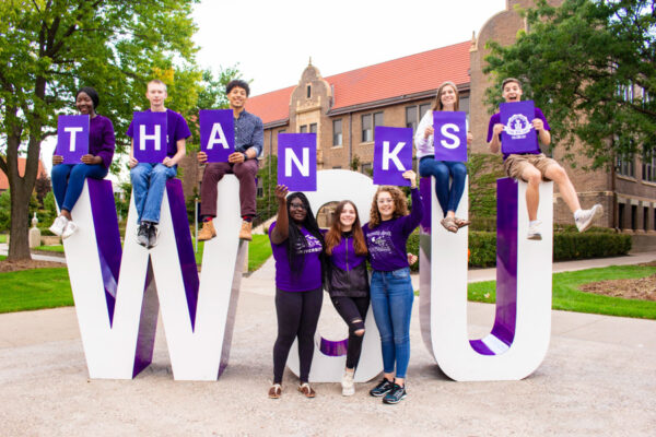 Students pose by the WSU letter holding signs that spell out 