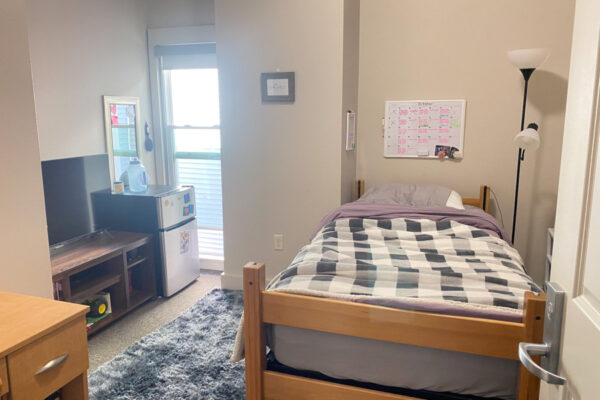 A bedroom in the WSU Sustainability House with a lofted bed, desk, mini fridge, and tv.