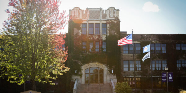 An exterior view of Somsen Hall with flags flying outside and ivy on the walls.